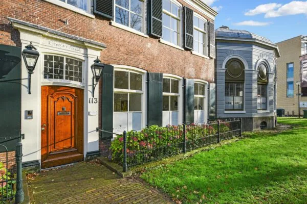 Vooraanzicht van een historisch herenhuis aan de Kleine Houtweg 113 met houten deur, hoge ramen en een goed onderhouden voortuin.